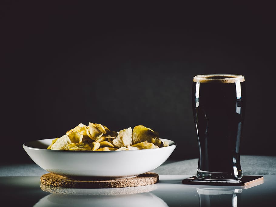 black beverage in clear drinking glass beside brown chips, closed HD wallpaper