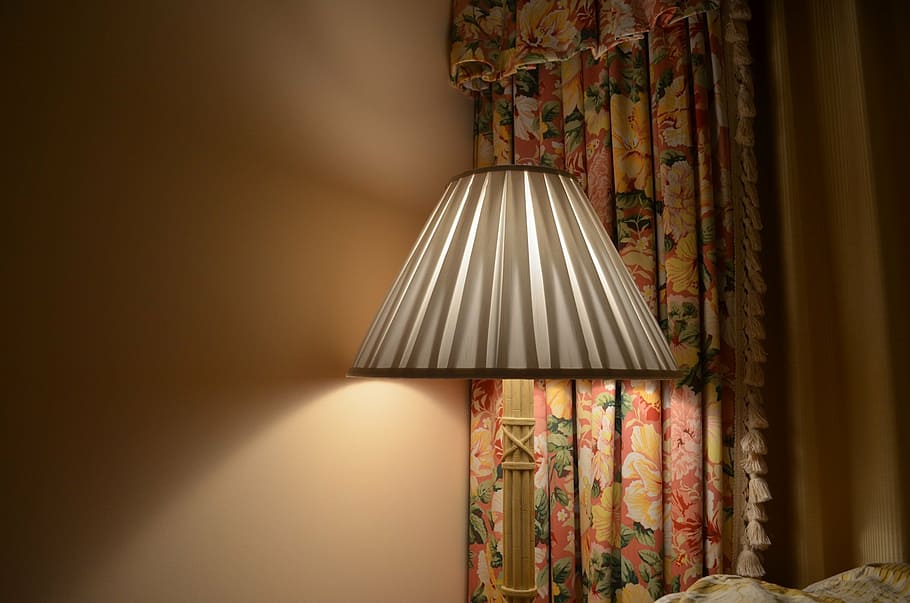 turned on black and gray table lamp beside bed in front of floral window curtain
