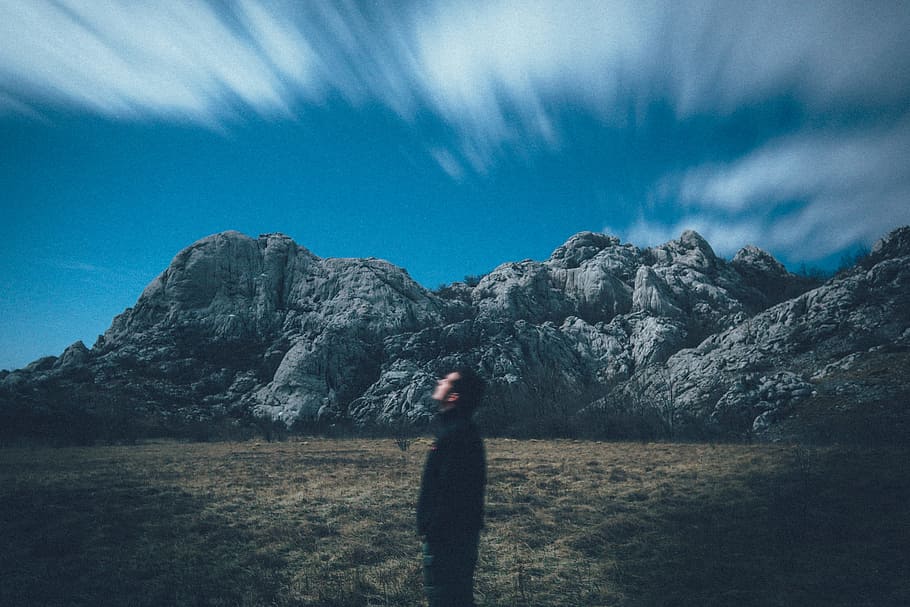 man looking up the sky located across the rock formation, man standing on field HD wallpaper