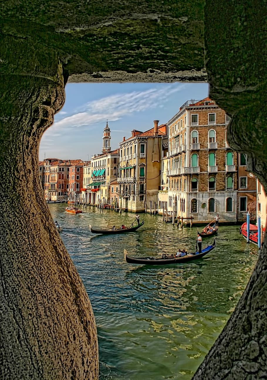 people riding on two black canoes, boats on green body of water near concrete buildings during daytime HD wallpaper