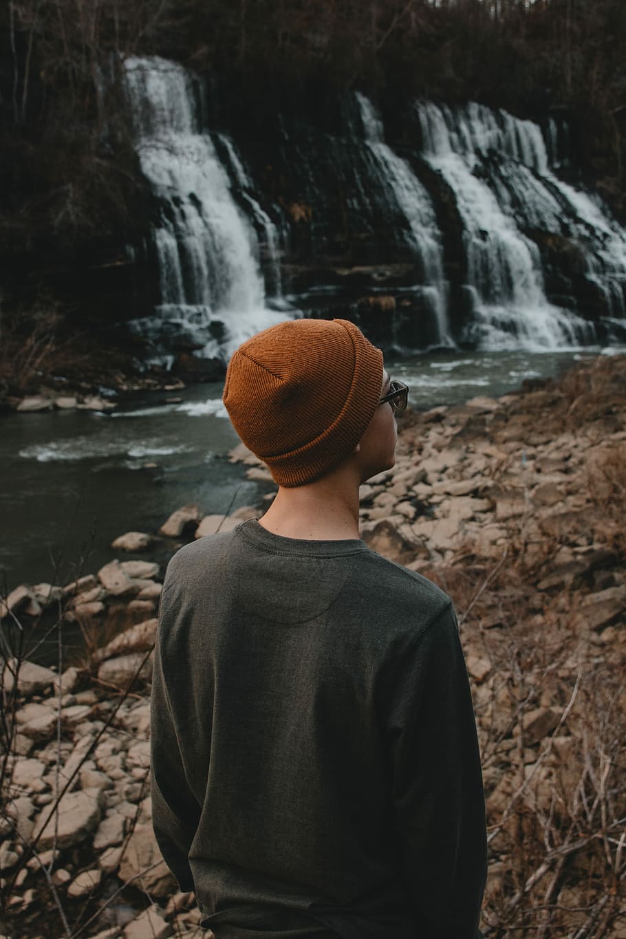person standing in front of water falls, person standing on rocky shore HD wallpaper