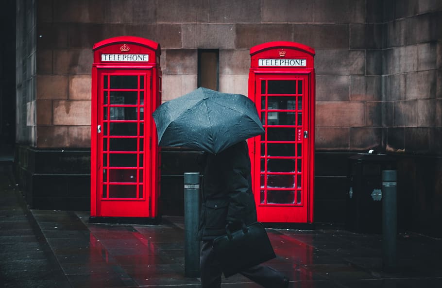 person under umbrella walking beside telephone booths, person wearing coat holding umbrella walking beside red telephone booths HD wallpaper