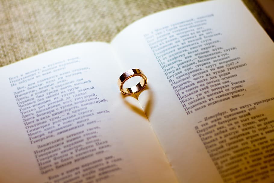 gold-colored wedding band on white book page, engagement, rings