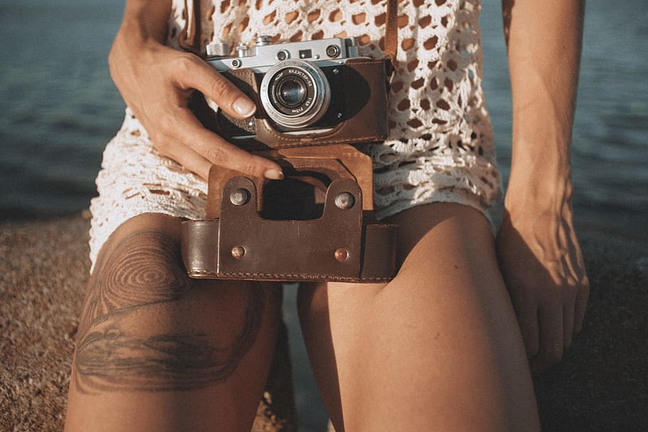 person holding camera near water, person with tattoo holding mirrorless camera