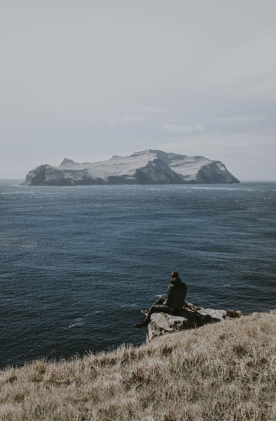man sitting on rock formation beside sea, man sitting on mountain cliff HD wallpaper