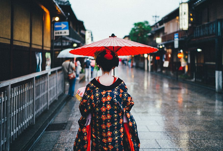 woman holding oil umbrella near on buildings, Geisha walking on street during rainy day