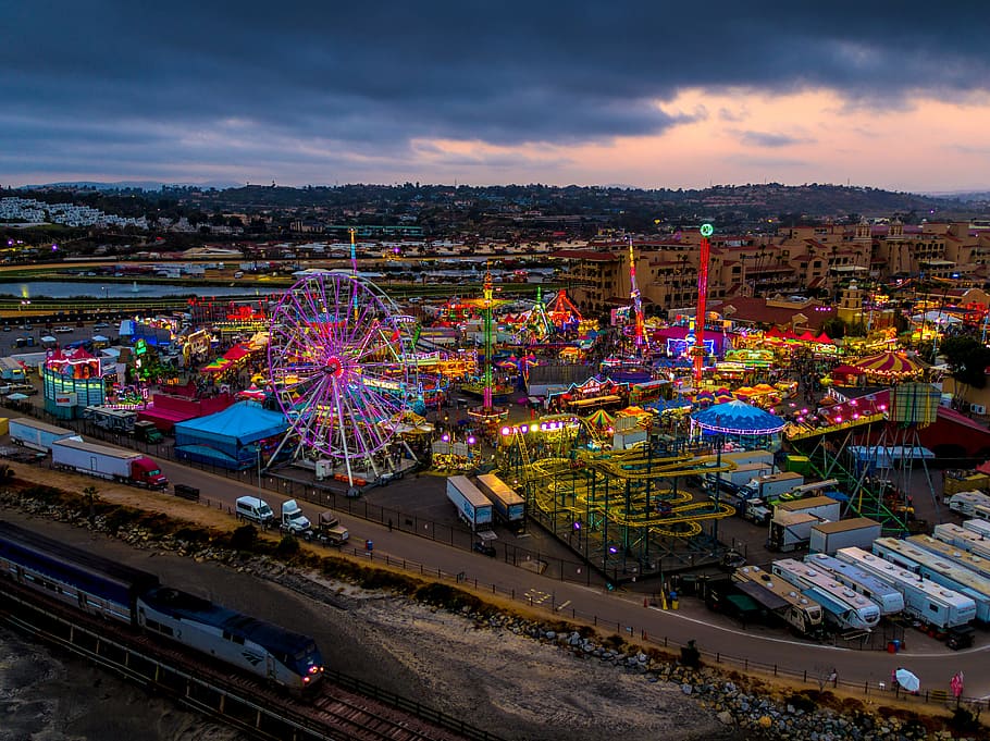 high-angle photography of multicolored amusement park beside train during daytime, aerial view carnival under gray sky during nighttime HD wallpaper