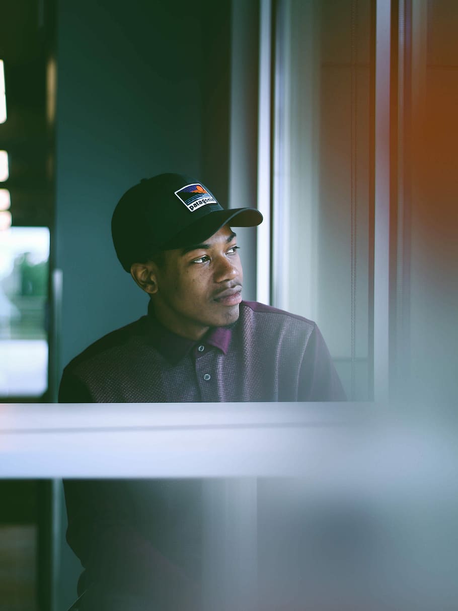 man wearing gray and purple polo shirt inside room, man wearing cap near window HD wallpaper