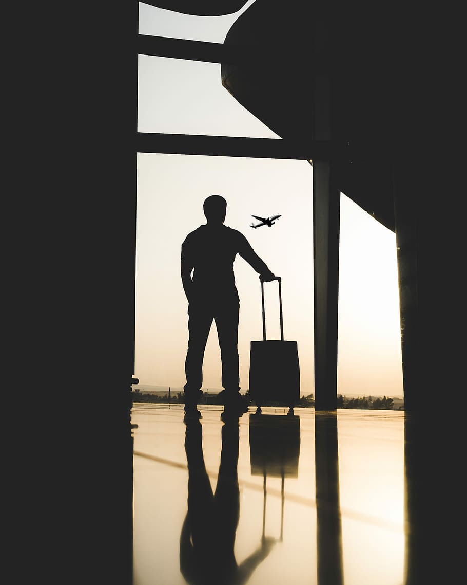 silhouette of man holding luggage inside airport, silhouette of man looking at the window of the airport