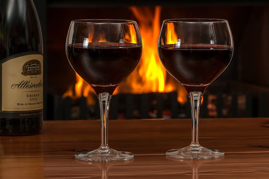 two clear long-stemmed drinking glasses, red wine, log fire HD wallpaper