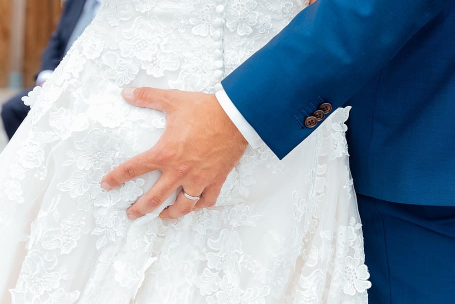 man wearing blue blazer holding woman wearing white bridal gown