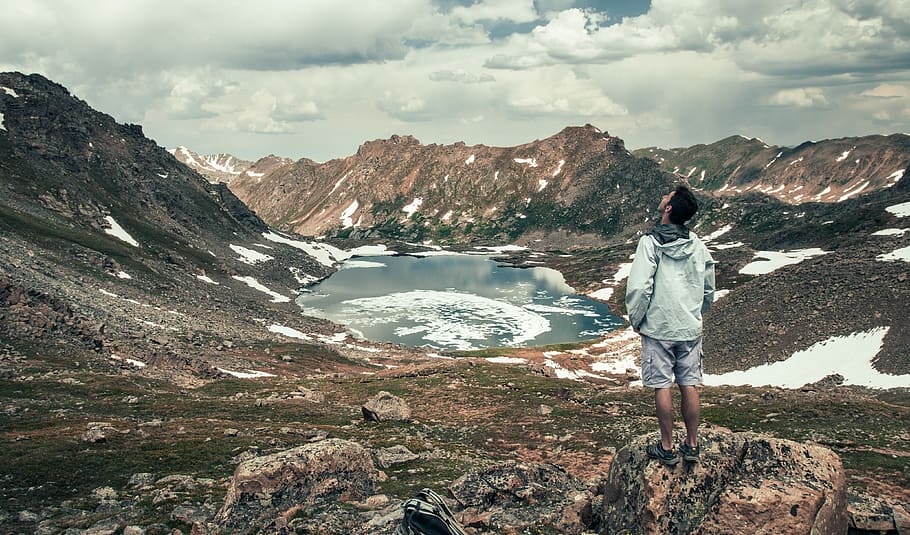 man standing facing at lake surround by mountains, man standing near body of water HD wallpaper