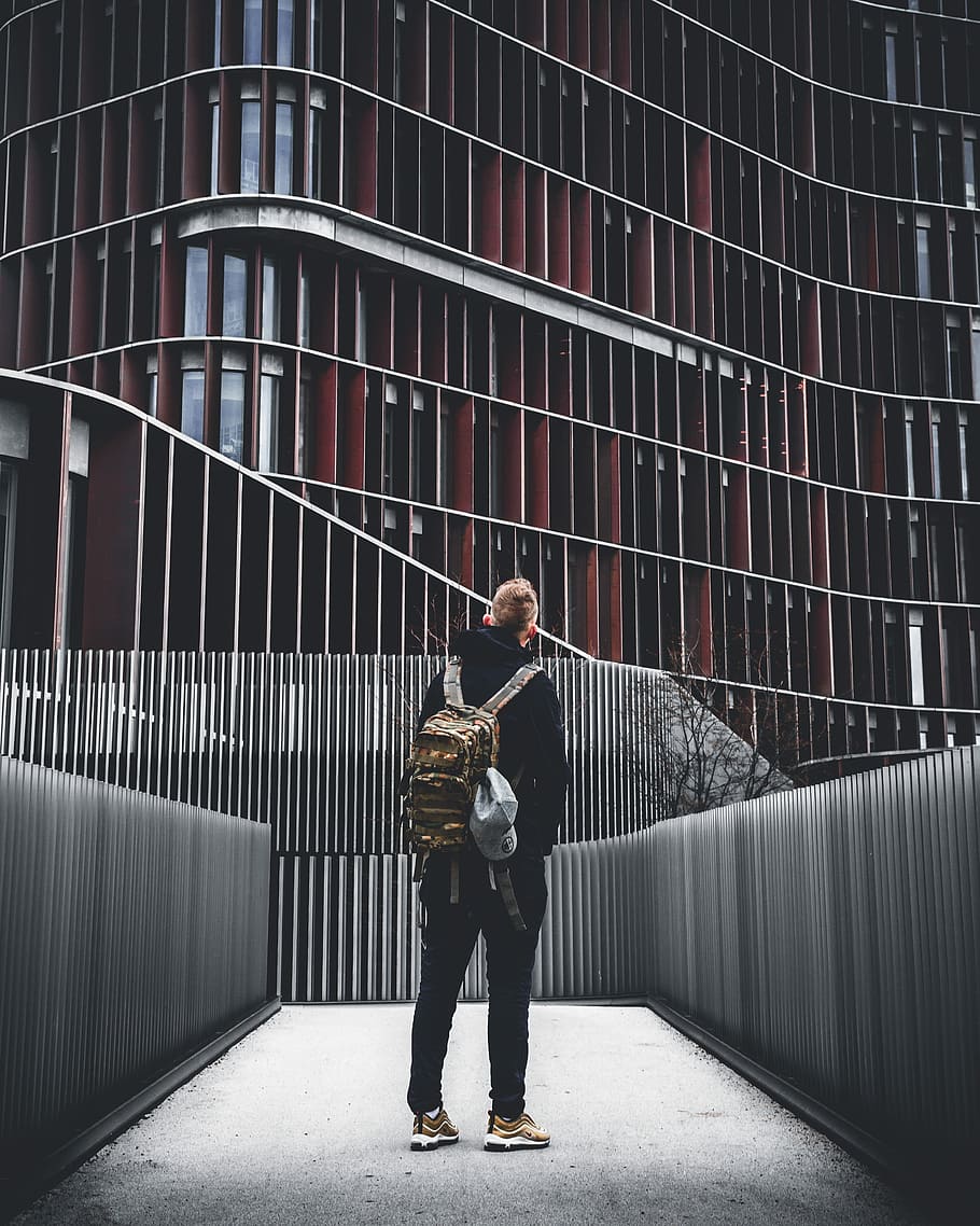 man standing under building, man wearing backpack looking an building, HD wallpaper