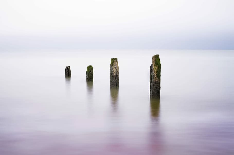 landscape photography of sea posts, four grey rocks on blue body of waters at daytime HD wallpaper