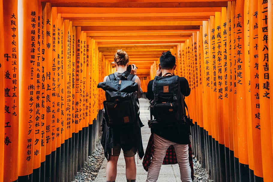 man and woman standing under orange kanji text print walls, photography of woman and man taking photo near orange wooden arc during daytime HD wallpaper