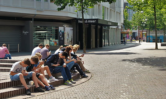 peoples sits on railings near building and tall trees at daytime HD wallpaper