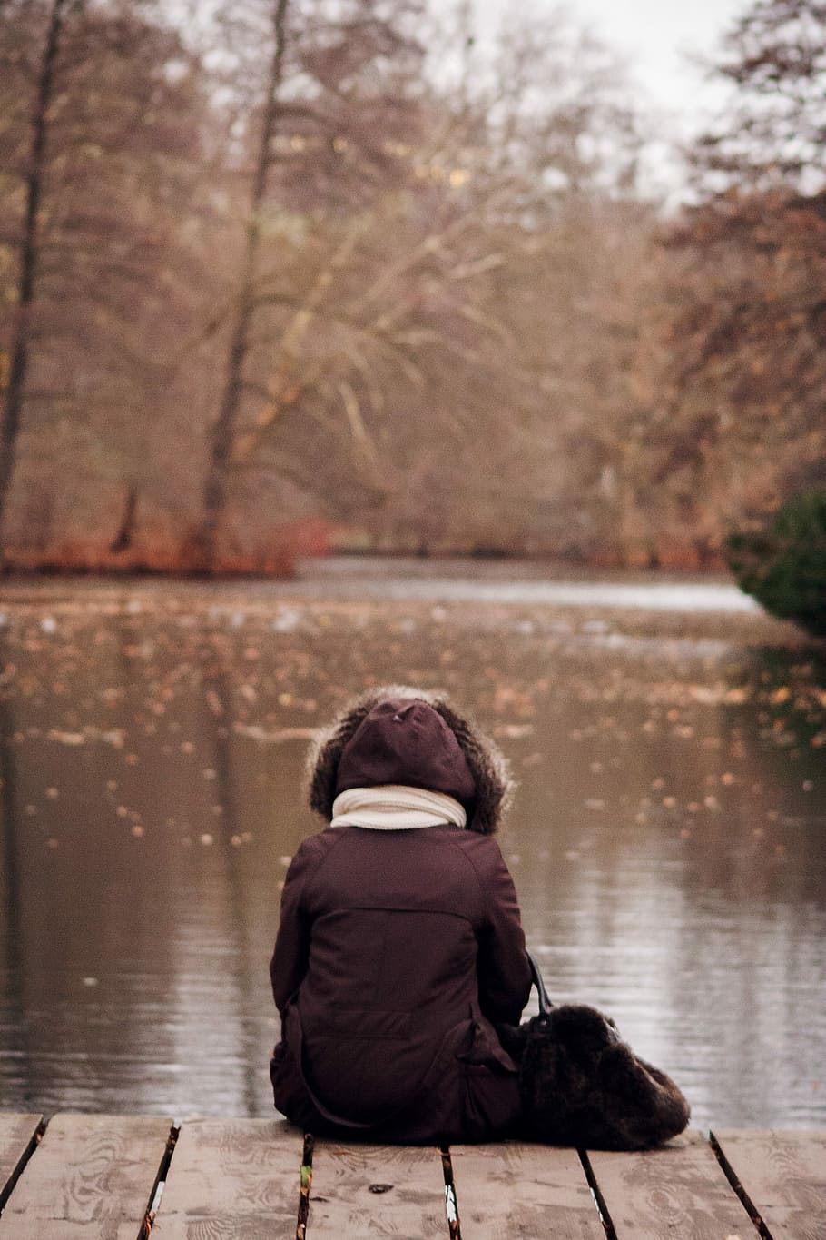 person in black coat sitting on wood above body of water, outdoors HD wallpaper