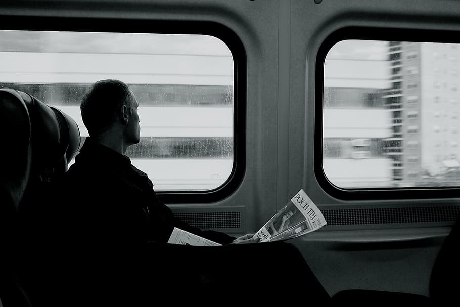 person riding passenger vehicle while holding newspaper, train