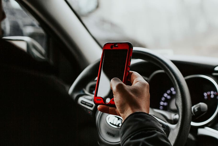person holding red smartphone sitting in front of vehicle steering wheel, person holding smartphone in front of steering wheel HD wallpaper