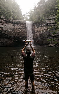 man holding drone facing waterfalls, man using his white drone HD wallpaper