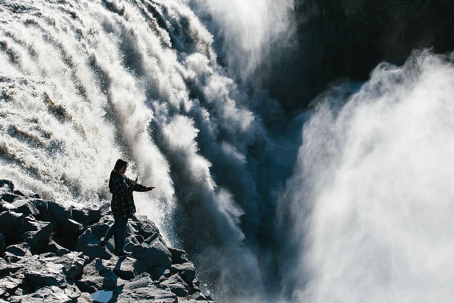 person standing waterfalls, woman standing on grey rocks on top of waterfalls during daytime HD wallpaper