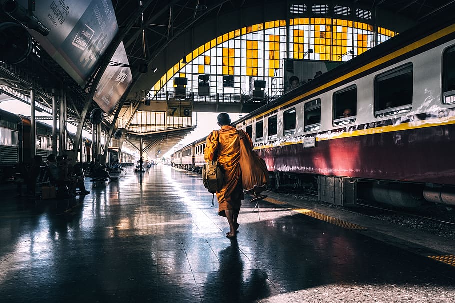 man walking on railway station platform near train, woman wearing yellow dupatta scarf walking on train station during daytime