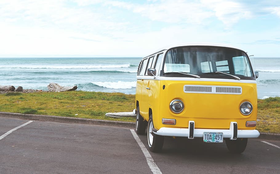 yellow Volkswagen T2 van on concrete road, yellow and white bus parked near sea shore under cloudy sky