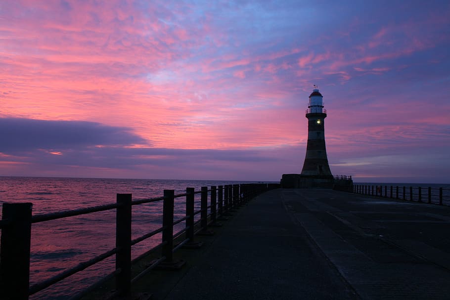 silhouette of lighthouse on wooden dock under pink and blue sky HD wallpaper