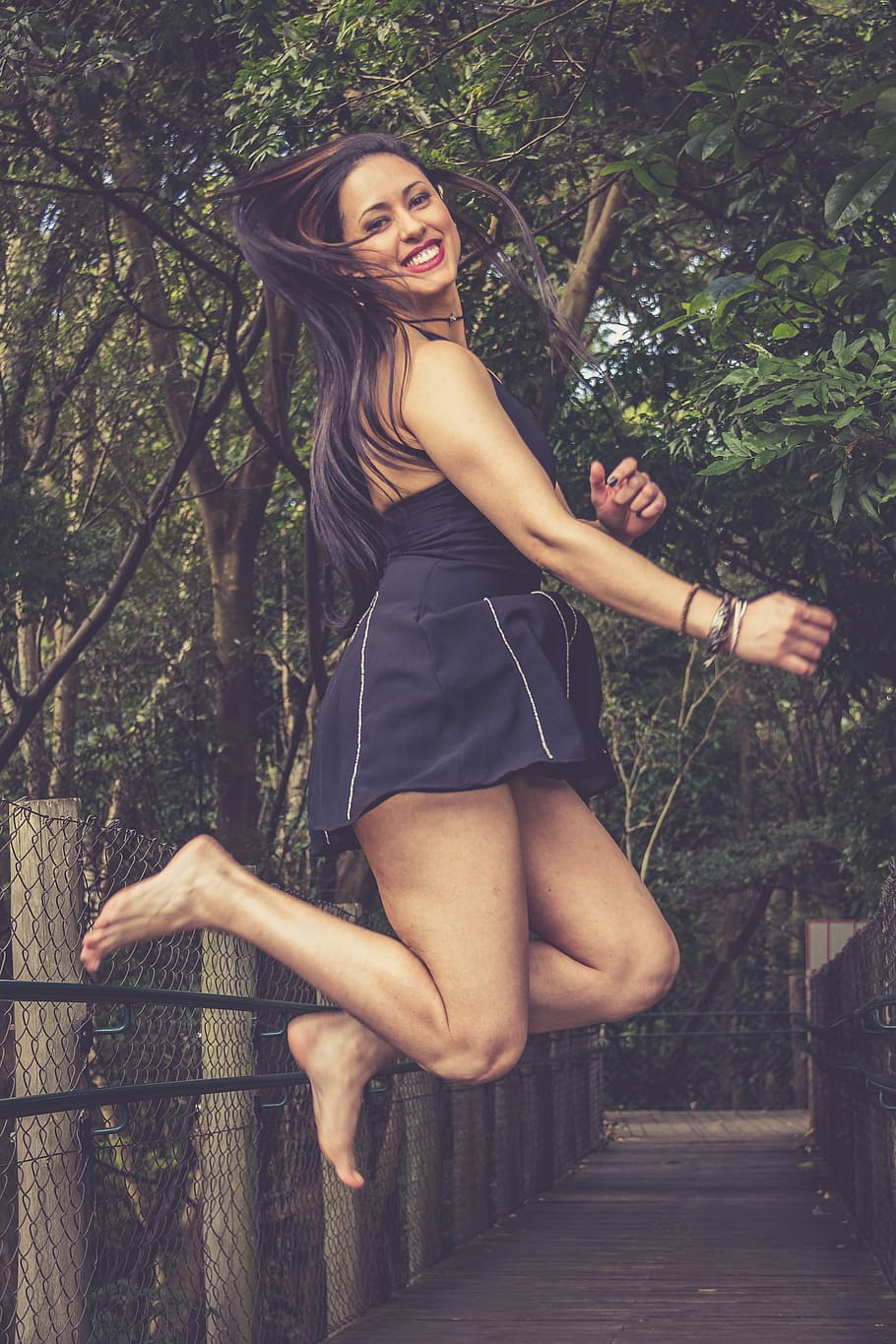 woman wearing black halter dress jumping under green trees HD wallpaper