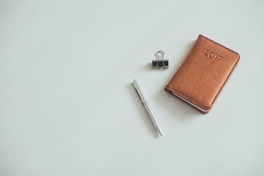 2017 brown planner beside clip and pen on white panel, notebook HD wallpaper