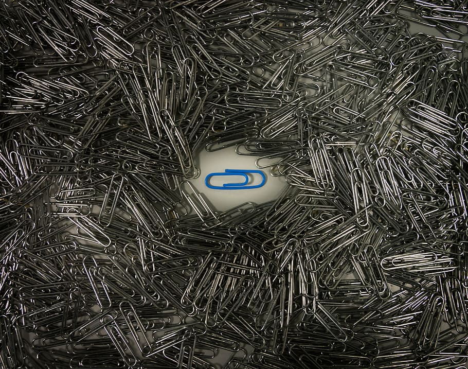 blue paper clip in the middle of pile of grey paper clips, background
