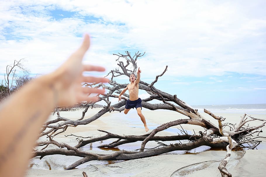 man jumping on driftwood, sea, clouds, branches, hands, people HD wallpaper