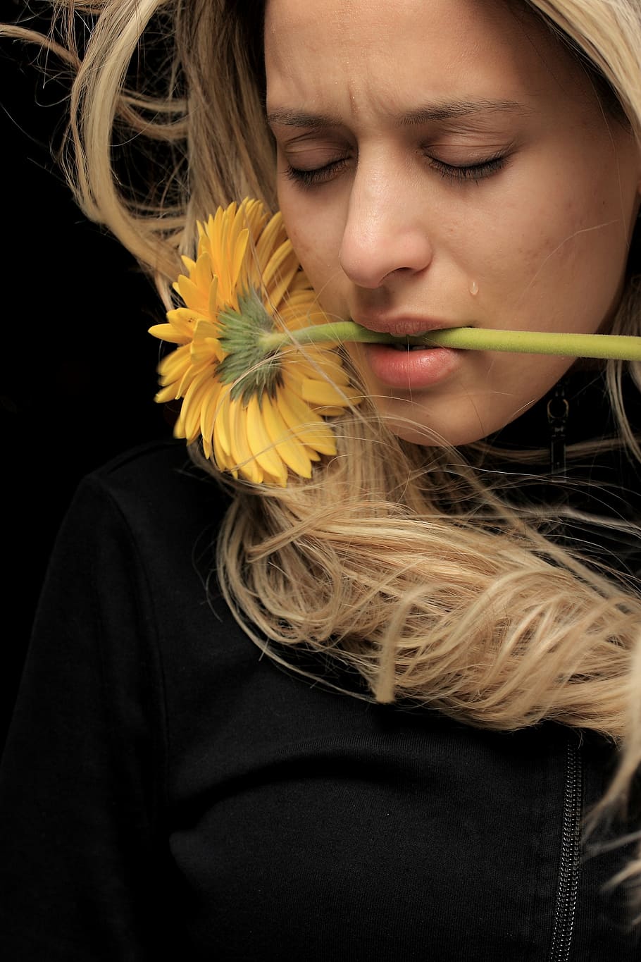 woman wearing black zip-up top biting yellow sunflower, model