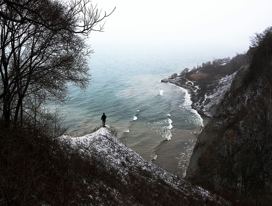 person standing on top of hillside looking on shoreline during daytime HD wallpaper
