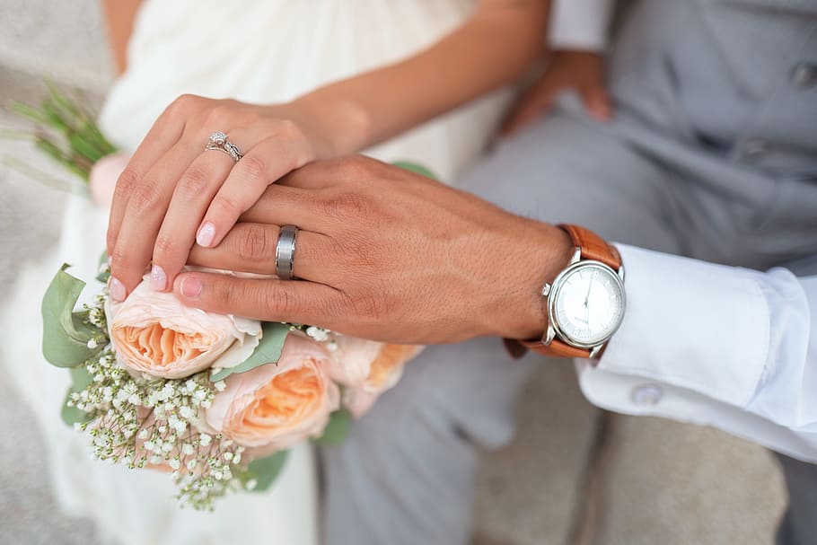 man and woman holding hands, female and male holding each others hand showing their wedding rings while touching flowers