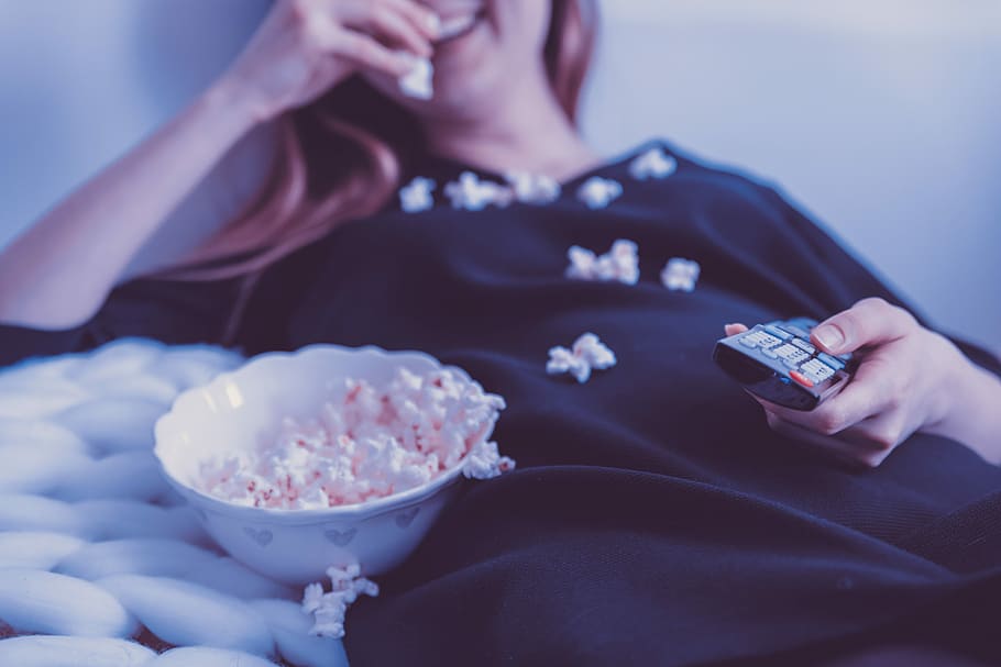 woman lying on bed while eating puff corn, woman in black long-sleeved dress eating popcorn while holding black remote control, HD wallpaper