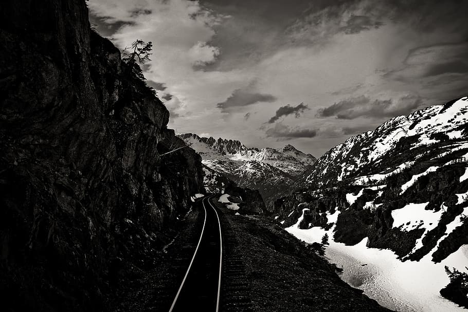 gray train rail beside snow covered mountain, grayscale photography of icy mountains