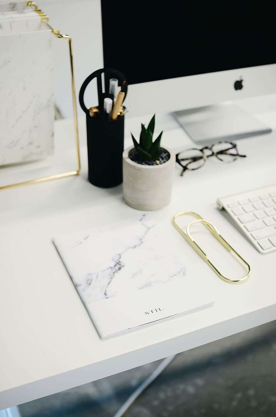 silver iMac and Magic Keyboard on ta ble near white printer paper, white and black book above white wooden table HD wallpaper