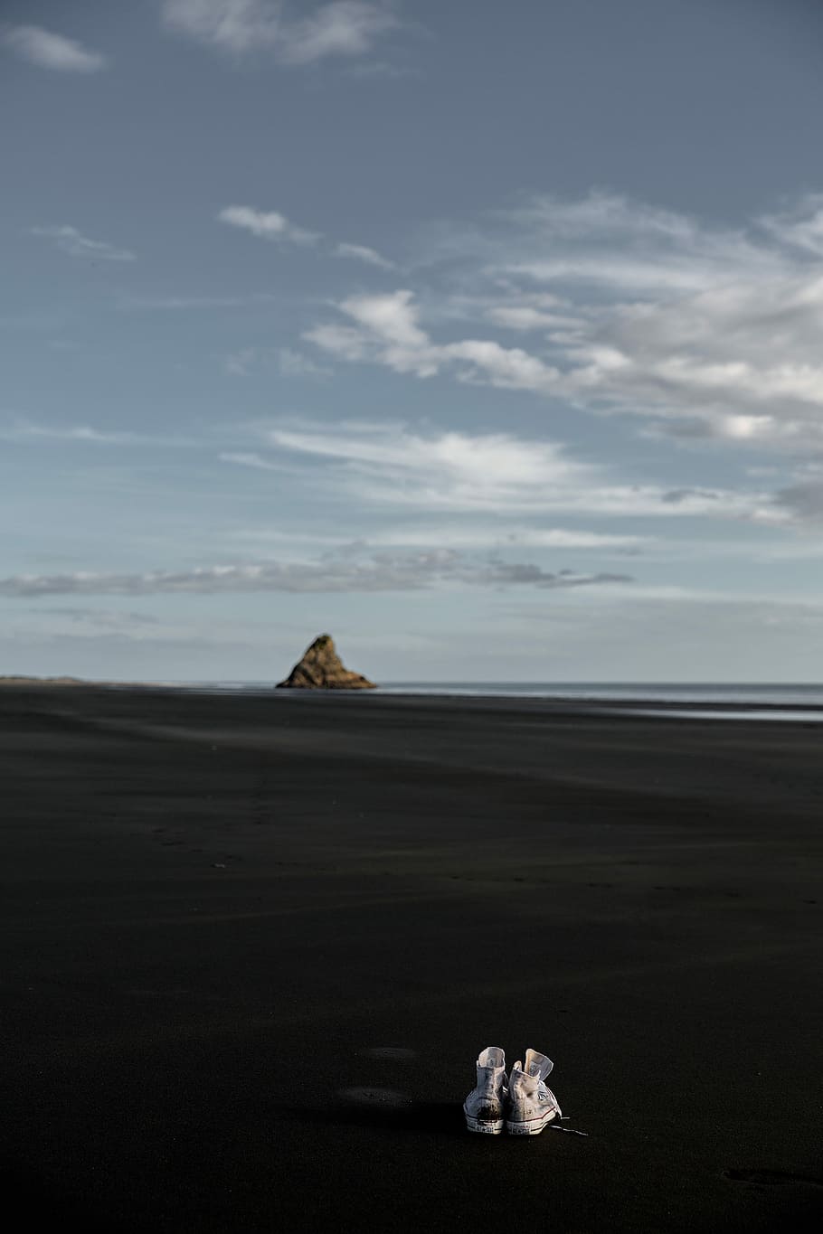 pair of sneakers on black sand, pair of white high-top sneakers on sand in front of rock formation and seawave under white clouds at daytime HD wallpaper