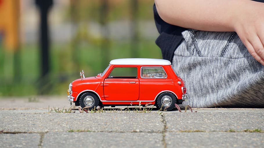 red and white 3-door hatchback scale model toy beside sitting person during daytime HD wallpaper