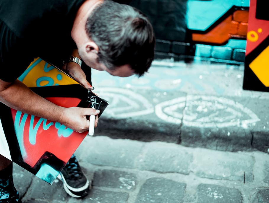 person writing something on black board, man bending while signing board during daytime HD wallpaper