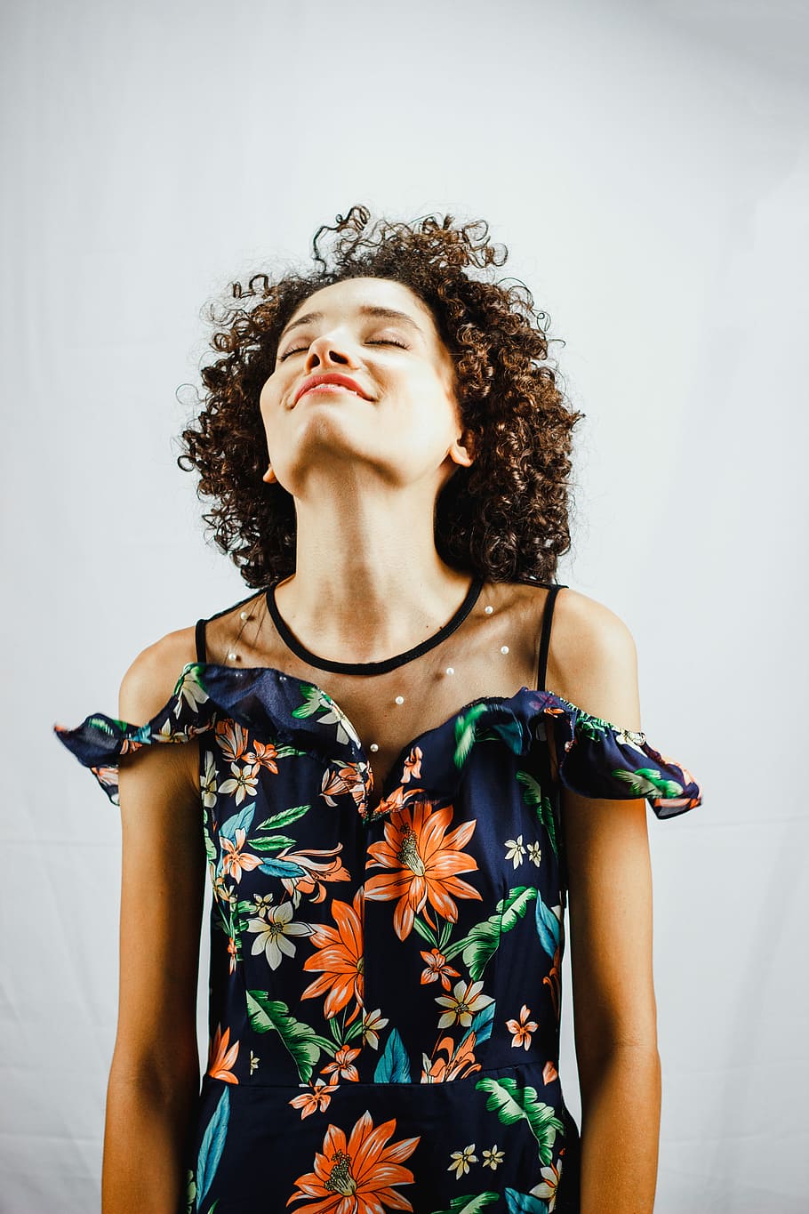 woman smiling while looking upwards, woman closing her eyes while standing near white wall HD wallpaper