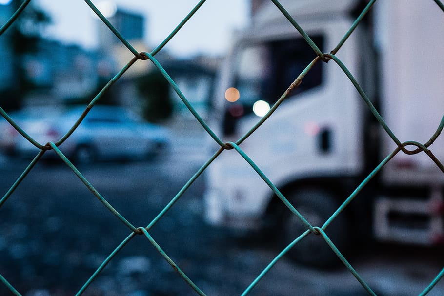selective focus photography of gray chain link fence, white delivery truck behind gray cyclone fence in tilt shift photography