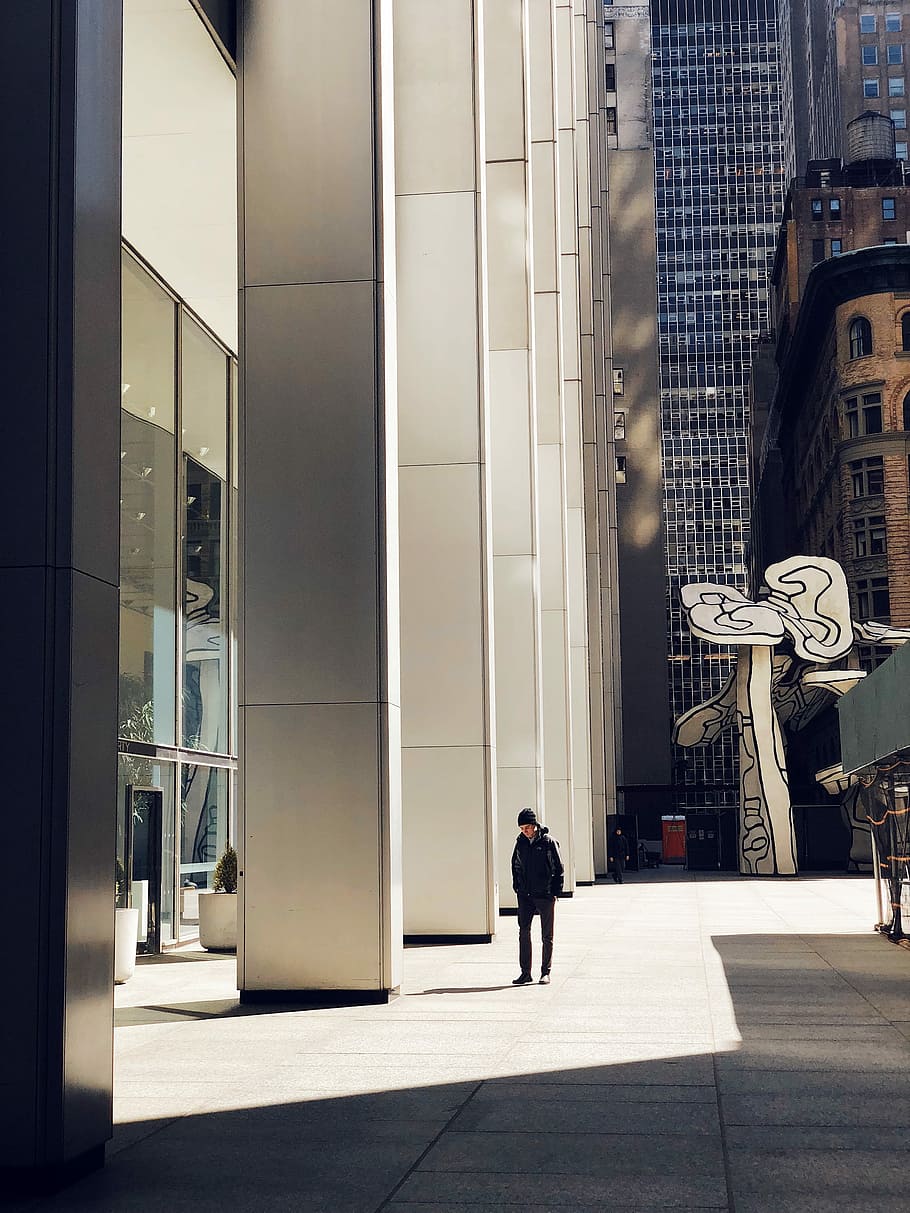 man walking near high-rise building, man standing on concrete pavement beside high building during daytime HD wallpaper