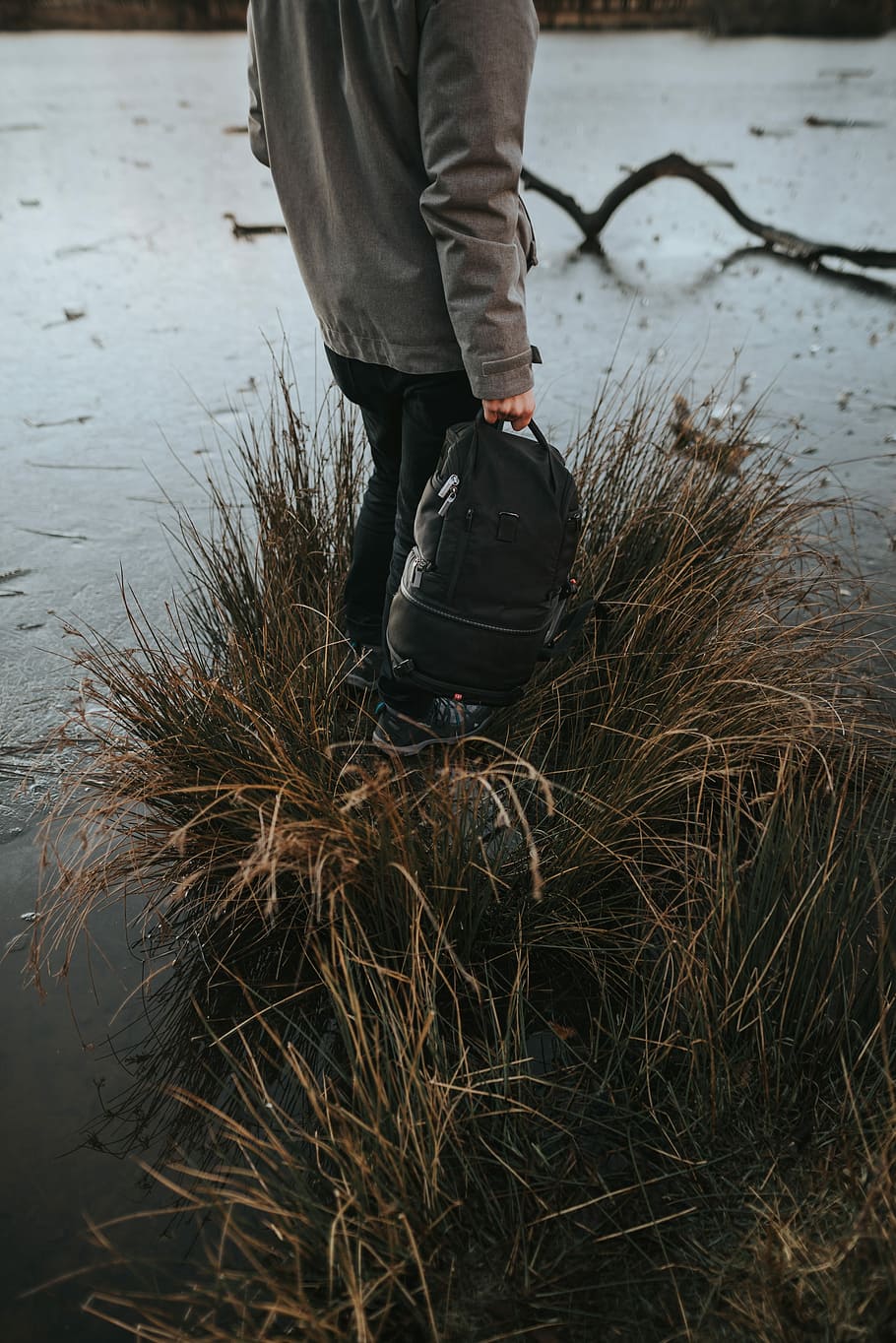 person carrying black backpack, person standing on brown grass holding backpack surrounded by water HD wallpaper