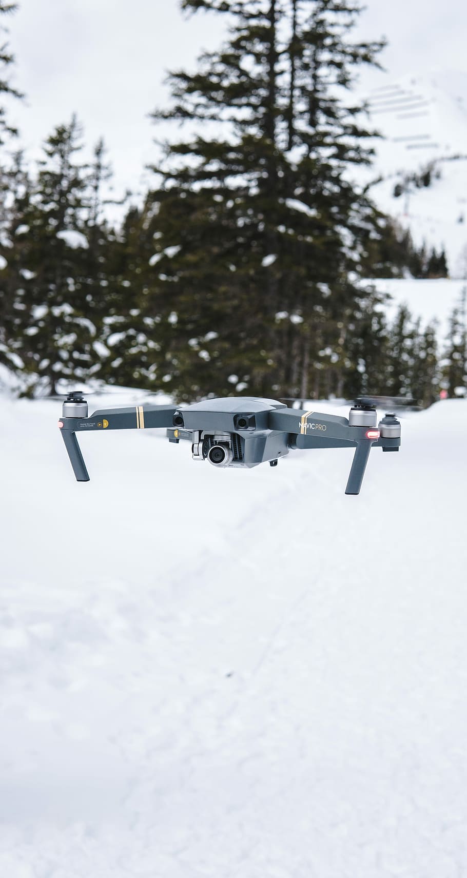 gray flying quadcopter near trees with snow, flying gray drone above snow ground with trees ahead at daytime HD wallpaper