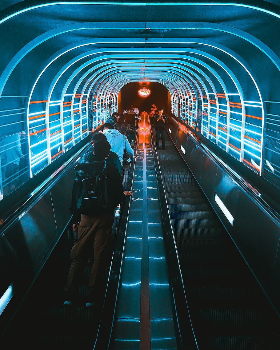 photo of people using escalators under blue LED lights, people standing on escalator inside the tunnel