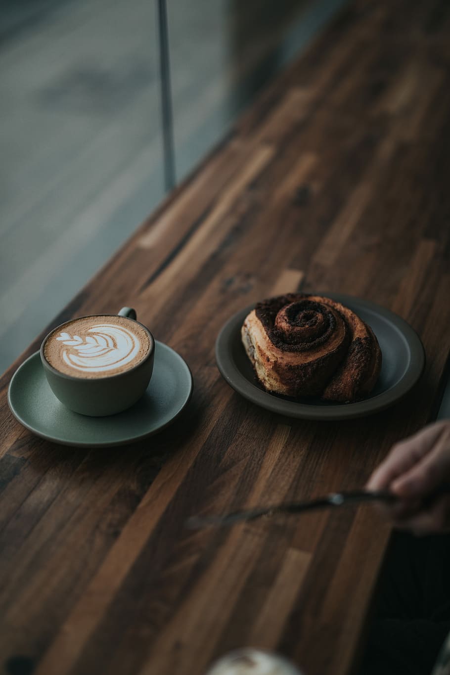 bread and latte on saucers, rolled bread on round black plate beside teacup filled with coffee on round gray ceramic saucer HD wallpaper