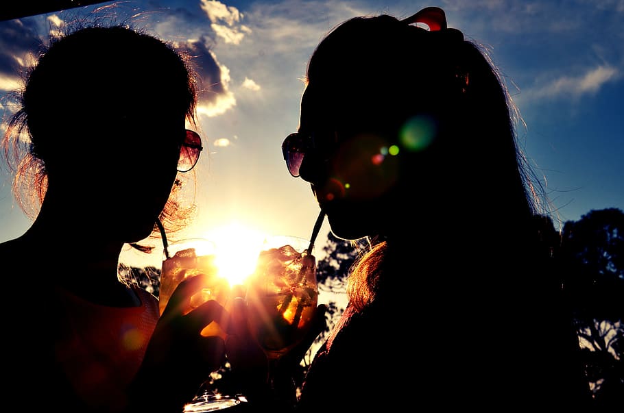 silhouette of two women zipping drinks during golden hours HD wallpaper