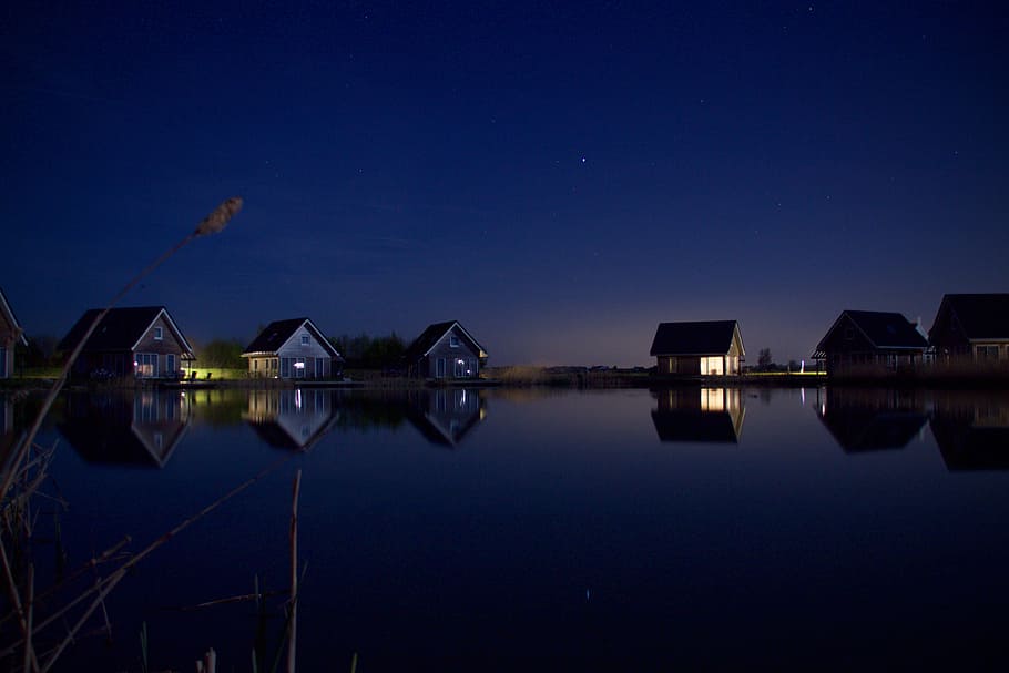 calm body of water near six houses and trees at night, six wooden houses near body of water during night time photo HD wallpaper